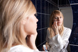 Fototapeta  - Blond young woman in bedroom applying makeup
