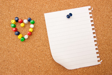 White note with many pushpins in a shape of a heart on corkboard