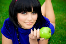 Young Beautiful Woman Lays On Green Field With Apple