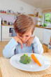 Kind sitzt vor Teller mit Gemüse