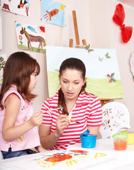 Child  painting with teacher in preschool.