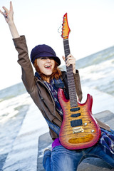 Poster - Young red-haired girl play on guitar at windy day.