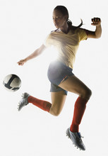 Mixed Race Soccer Player Kicking Soccer Ball In Mid-air