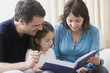 © REB Images/Blend Images - Hispanic parents reading book to daughter