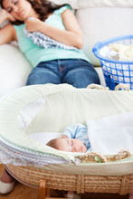 Cute Baby Sleeping In His Cradle With His Mother Lying On Sofa