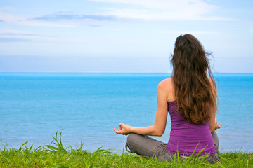 Beautiful fit young woman mediating by the ocean