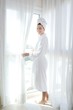 © lunamarina - Bathrobe woman sunny window white curtains