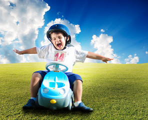 Happy kid on green meadow driving a car