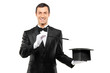 Magician in a black suit holding an empty top hat and magic wand