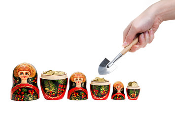 Three Matryoshkas full of coins and hand holding shovel