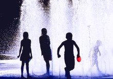 Silhouettes Of Children Playing In A Fountain