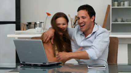Lovely happy couple looking at the laptop sitting at a table