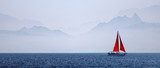 Yacht with a red sail on a mountain background