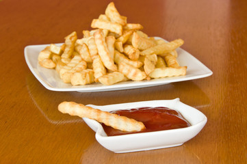 Single french fry with ketchup and  plate of fries