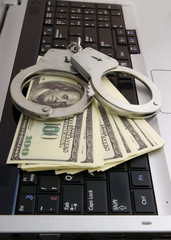 Hacker concept, handcuffs and money on laptop