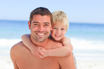 Canvas Print - Smiling father having son a piggyback at the beach