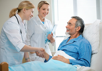 doctor shakes hands with patient in hospital bed