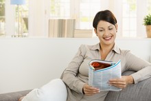 Happy Woman Reading Newspaper On Sofa