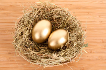 Wall Mural - Three golden hen's eggs in the grassy nest on the wooden table