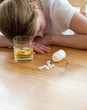 close up of pills and alcohol with suicidal woman to background