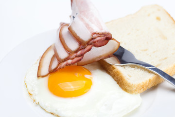 bacon with  fried  eggs on a plate, fork and bread isolated on w