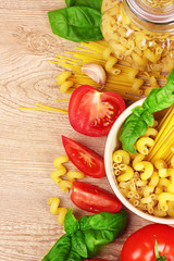 spaghetti with basil leaves, tomatoes and pepper on a yellow bac