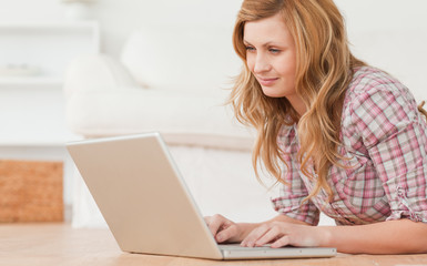 Wall Mural - Blond-haired woman working on her laptop lying down on the floor