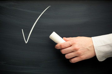 chalk tick and hand against blackboard background