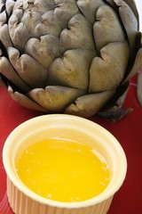 Steamed artichoke with melted butter on a red ceramic plate