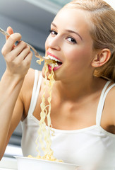 Wall Mural - Happy smiling young blond woman eating spaghetti indoors