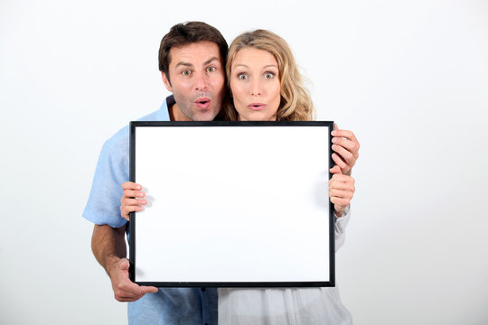 Shocked couple stood with blank message board