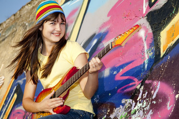 Beautiful brunette girl with guitar and graffiti wall at backgro