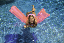 Young Woman In Pink Bikini Playing In A Pool On A Pink Float
