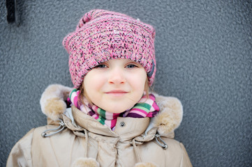 Wall Mural - Smiling child girl wearing pink knitted hat and striped scarf