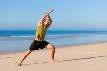 Wall Mural - Young sportive man doing gymnastics on the beach