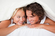 © WavebreakmediaMicro - Couple under a duvet with a knowing smile