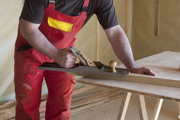 carpenter works on a wood house with a planer