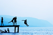 Silhouettes Of Kids Who Jump Off Dock On The Lake