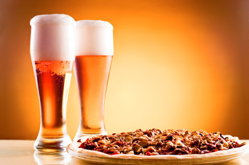 Two glass of beer and pizza over yellow background