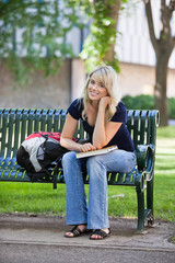 Wall Mural - Young female student sitting on bench