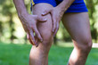 Schmerzen und Verletzung am Knie - Sportlicher Mann tastet mit 2 Händen sein Knie ab.