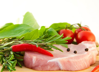 Meat, tomatoes, a basil and pepper against a wooden board.