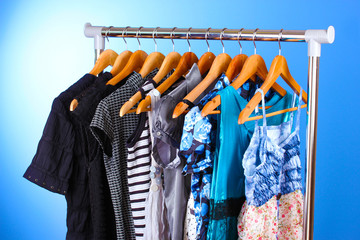 Wall Mural - different clothes on wooden hangers on blue background