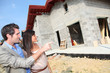 © goodluz - Happy couple standing in front of house under construction