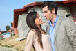 © goodluz - Happy couple standing in front of house under construction