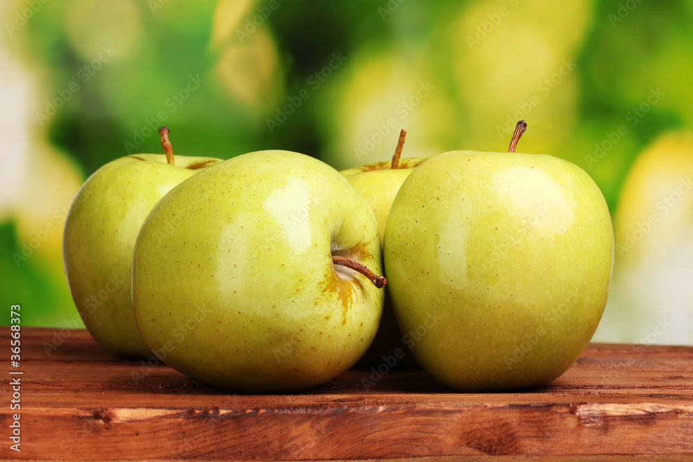 juicy green apples on wooden table on green background