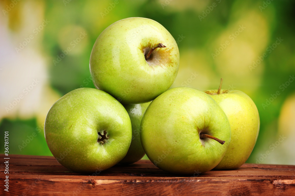 juicy green apples on wooden table on green background