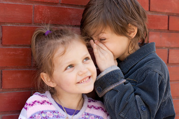 two kids sharing a secret. little boy whispering in little girl ear