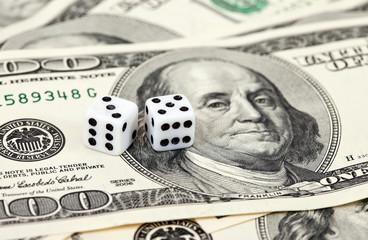 Two dice laying over a pile of money