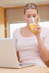 Poster - Portrait of a young woman using a laptop while drinking juice